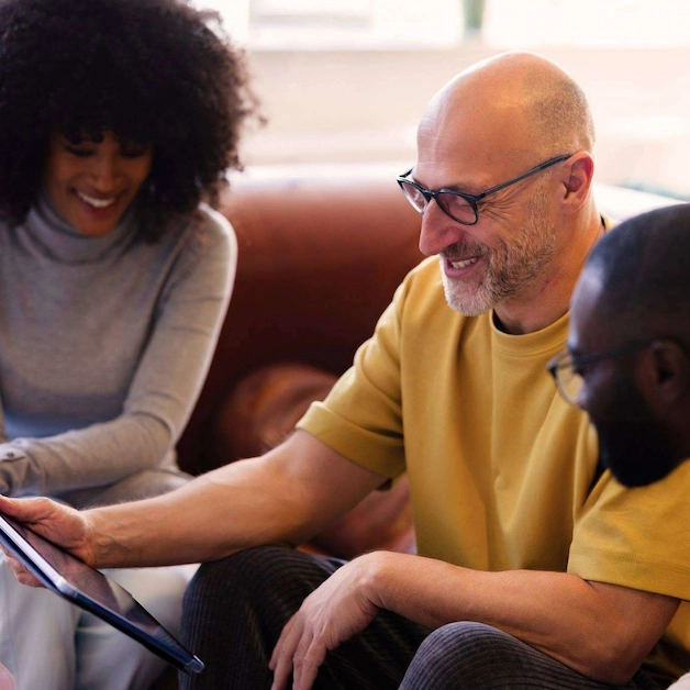 Three people on a sofa smiling and looking at a tablet